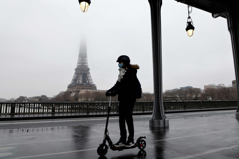 In this file photo taken on January 27, 2021 A woman rides a scooter in Paris in front of the Eiffel tower whose top disappears in the fog. Photo by Ludovic MARIN / AFP