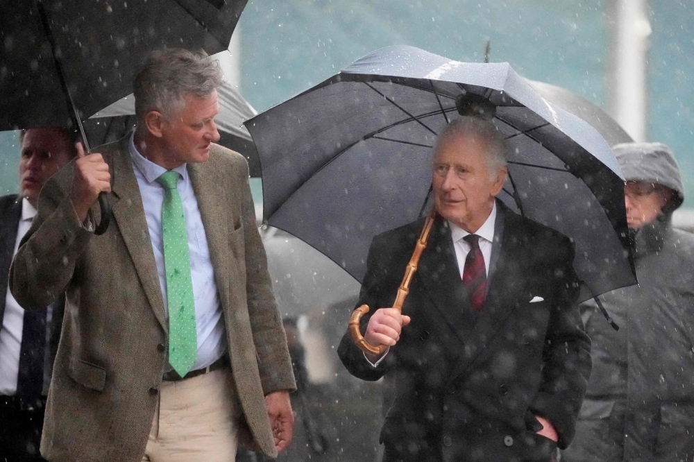 Britain's King Charles III (right) uses an umbrella to protect against the pouring rain as he walks with manager of the Oekodorf Brodowin eco-village Ludolf von Maltzan after visiting the village including an organic farm with milking parlour and cow shed, in Brodowin, eastern Germany, on March 30, 2023.  (Photo by Matthias Schrader / POOL / AFP)