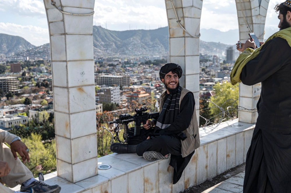 A Taliban security personnel take pictures of his colleague using a mobile phone at the Wazir Akbar Khan hilltop overlooking the Kabul city on April 4, 2023. (Photo by Wakil Kohsar / AFP)