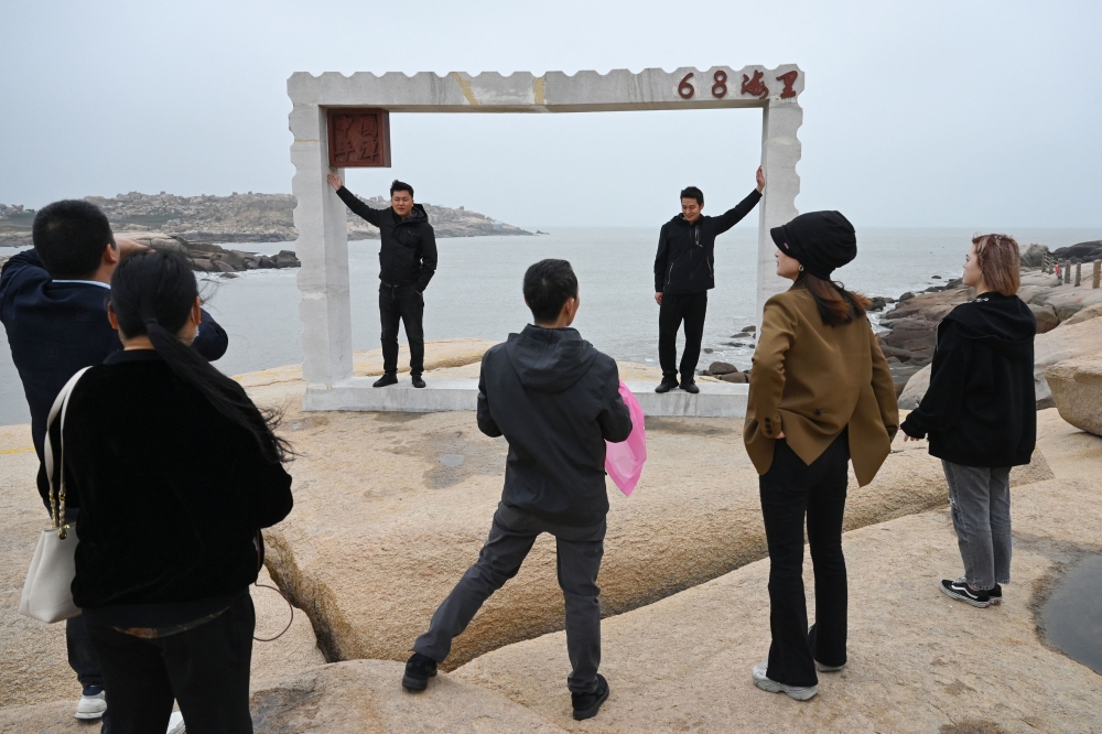 Chinese tourists pose for photos in front of the Taiwan Strait, on the coast of Pingtan island, the closest point to Taiwan, in China's southeast Fujian province on April 6, 2023. (Photo by Greg Baker / AFP)