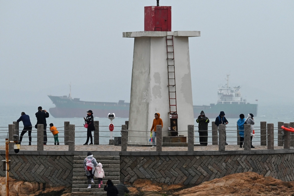A cargo sails in the Taiwan Strait, behind tourists on a lighthouse on Pingtan island, the closest point to Taiwan, in China's southeast Fujian province on April 6, 2023. (Photo by GREG BAKER / AFP)