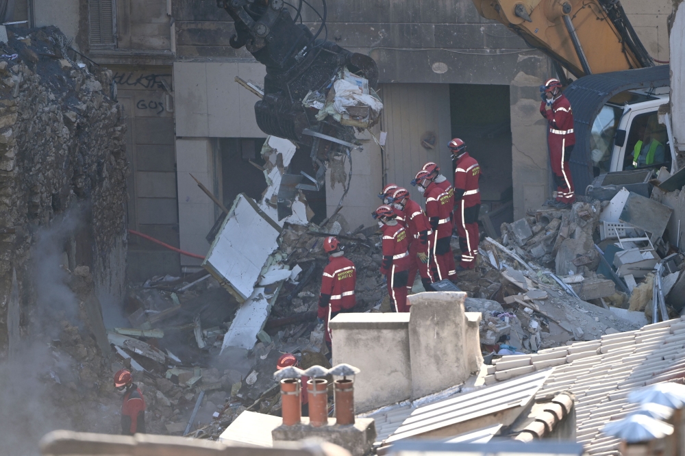Firefighters stand aside as an excavator clears rubble at 'rue Tivoli' after a building collapsed in the street, in Marseille, southern France, on April 9, 2023. Photo by CLEMENT MAHOUDEAU / AFP