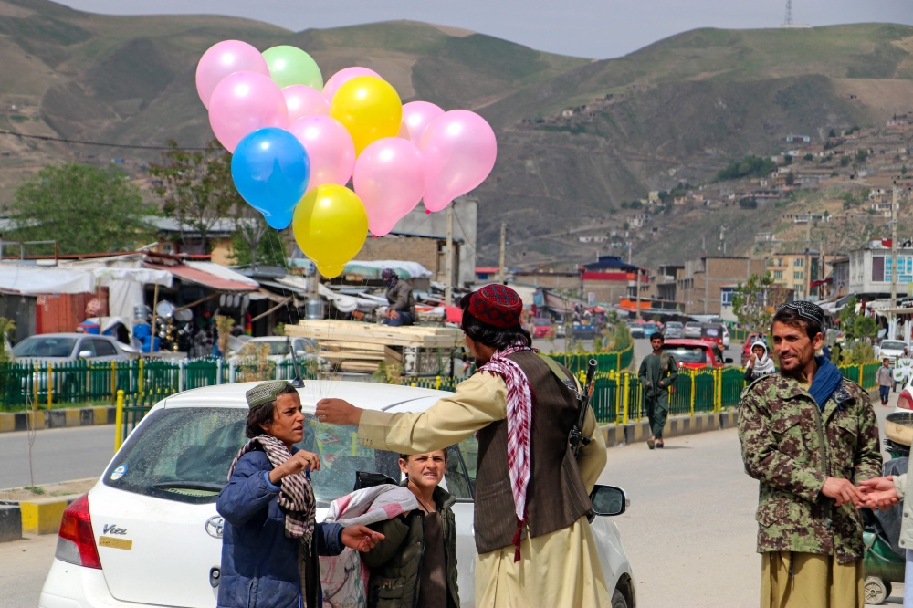 An Afghan boy selling balloons talks to a Taliban security personnel along a street in Fayzabad district of Badakhshan province on April 10, 2023. (Photo by OMER ABRAR / AFP)