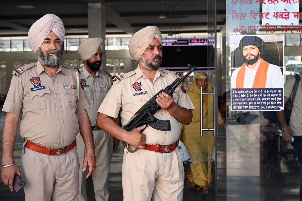 Punjab police stand guard beside Amritpal Singh's poster at a railway station in Amritsar on April 23, 2023. Photo by Narinder NANU / AFP)
