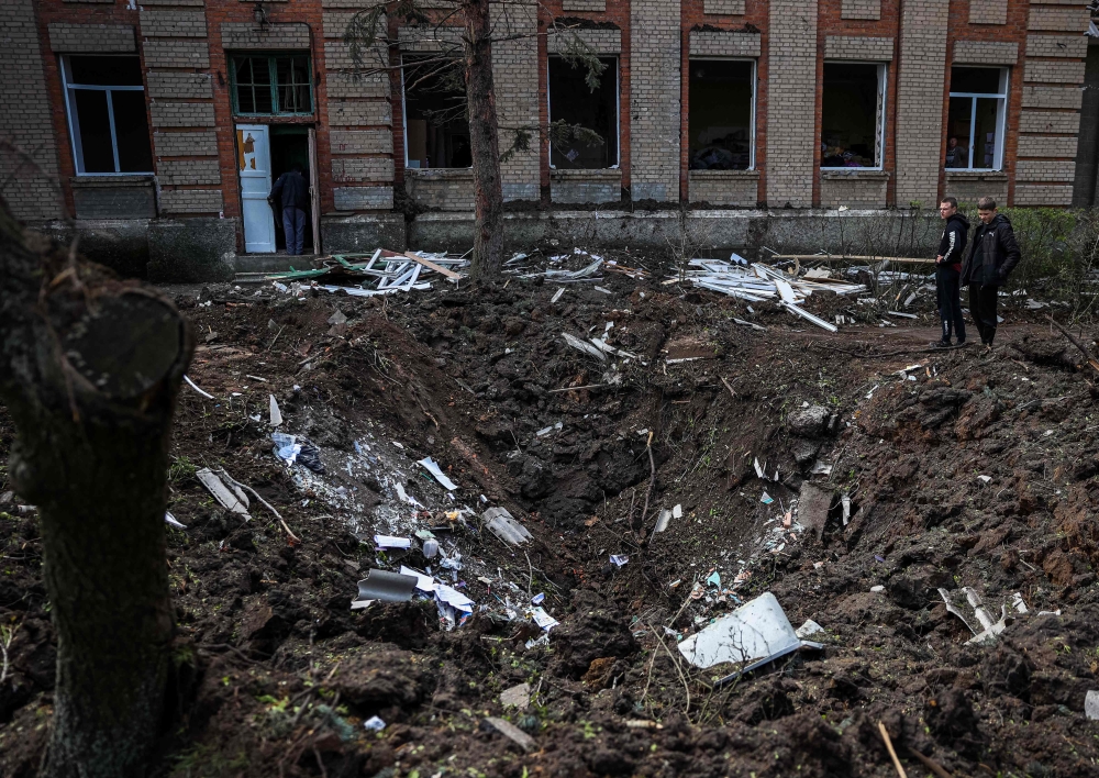 Teenagers stand next a crater left by a missile strike in front of a school building in Kramatorsk, in the Donetsk region on April 24, 2023, amid the Russian invasion of Ukraine. Photo by Anatolii STEPANOV / AFP