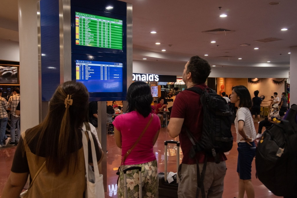 Passengers look at a screen showing flight information at terminal 3 of Ninoy International Airport in Pasay, Metro Manila on January 1, 2023. (Photo by KEVIN TRISTAN ESPIRITU / AFP)

