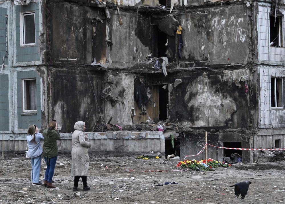 People pay their respects in front of a damaged multistory residential building, where a Russian strike killed 23 people, in Uman, Cherkasy region, on April 30, 2023. (Photo by Genya Savilov / AFP)