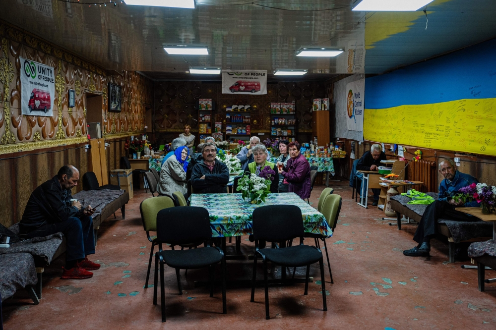 Local residents sit in a volunteer-run shelter, providing access to laundry and bathroom facilities where they can warm up, charge their phones, drink hot tea and receive humanitarian aid in the town of Orikhiv, in the Zaporizhzhia region, on May 7, 2023, amid the Russian invasion of Ukraine. (Photo by Dimitar Dilkoff / AFP)