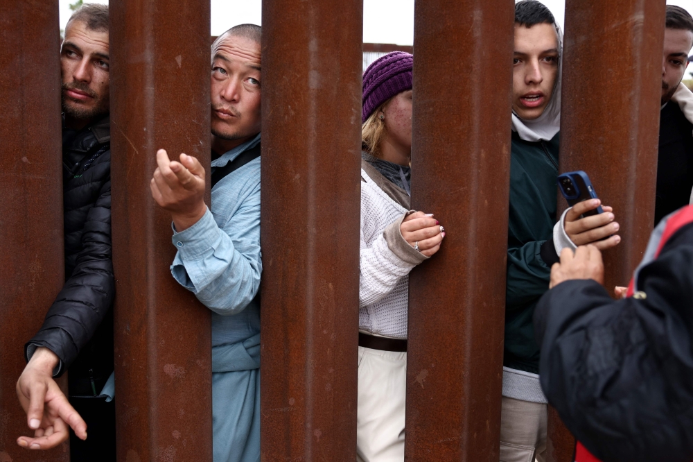Immigrants seeking asylum in the US, who are stuck in a makeshift camp between border walls between the US and Mexico, reach through the border wall as volunteers offer assistance on the other side on May 12, 2023 in San Diego, California. Mario Tama/Getty Images/AFP 