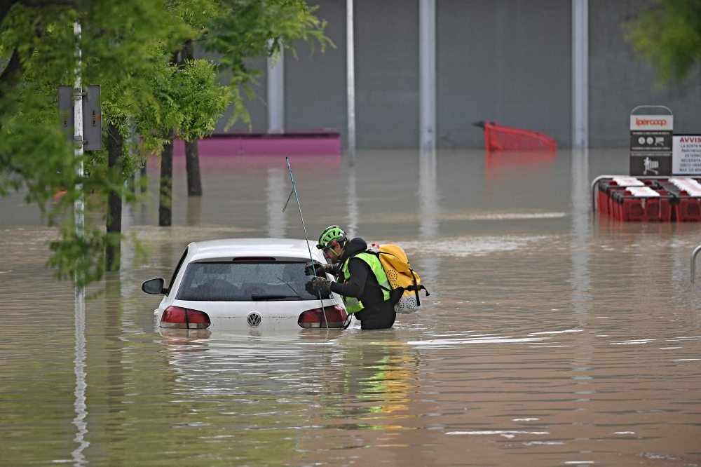 A speleological alpine rescuer looks in a car for missing persons near a supermarket in a flooded area in Cesena on May 17, 2023. Photos by Alessandro SERRANO / AFP