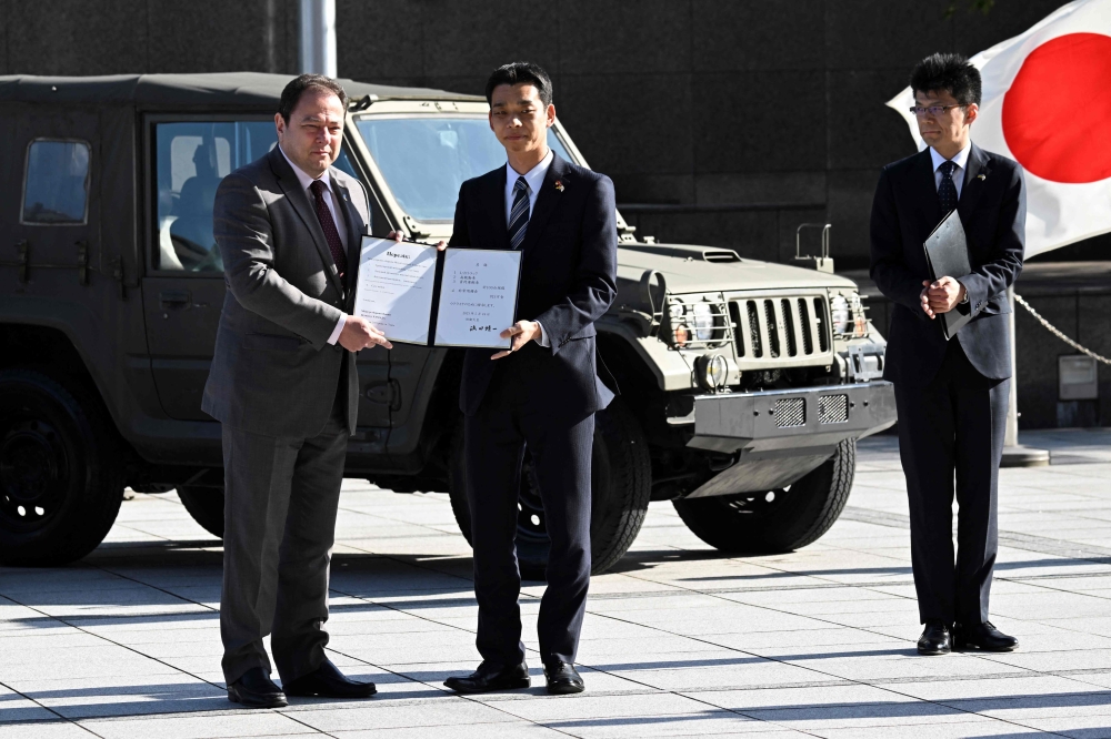Japan's State Minister of Defence Toshiro Ino (C) and Ukrainian Ambassador to Japan Sergiy Korsunsky (L) pose with a list of Japanese Self-Defense Force vehicles that were handed over to Ukraine, during a ceremony at the Defence Ministry in Tokyo on May 24, 2023. Photo by Kazuhiro NOGI / AFP