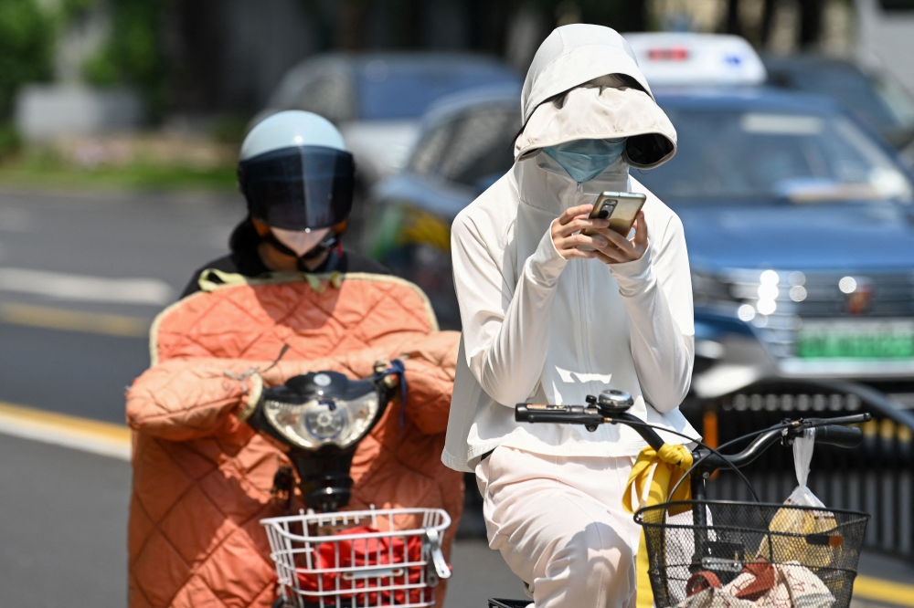 A woman wearing sun protective clothing commutes on a bicycle amid hot weather in Shanghai on May 29, 2023. Photo by AFP