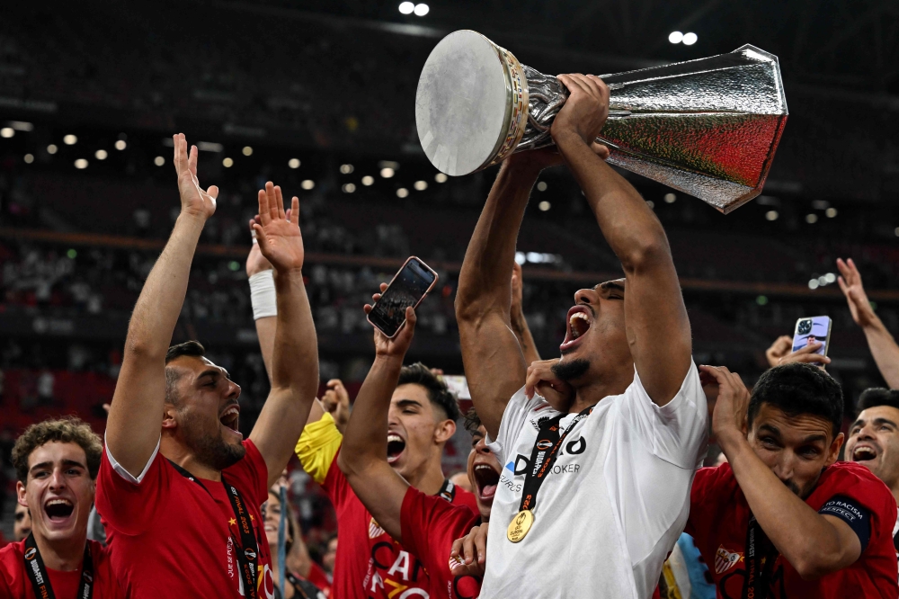 Sevilla's French defender Loic Bade (R) carries the trophy as he celebrates with the fans after winning the UEFA Europa League final football match between Sevilla FC and AS Roma at the Puskas Arena in Budapest on May 31, 2023. (Photo by VLADIMIR SIMICEK / AFP)