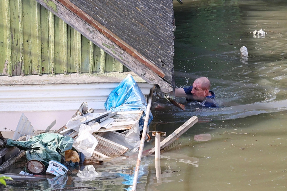 A local resident swims by a house in a flooded area in Kherson on June 7, 2023, following the destruction of Kakhovka hydroelectric power plant dam. (Photo by Olexander Kornyakov / AFP)
