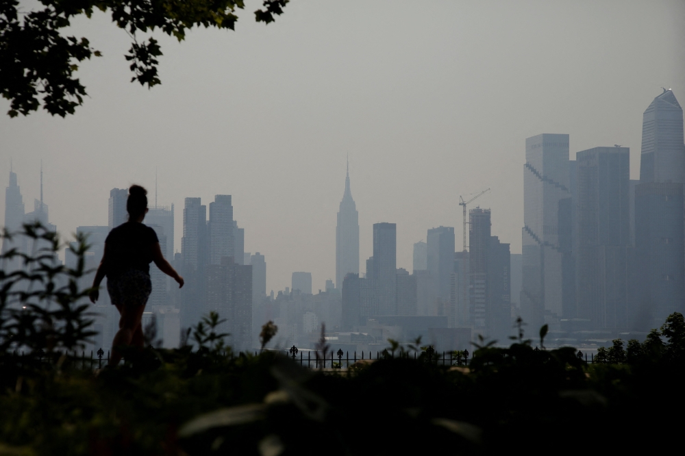 The Manhattan skyline is seen across the Hudson river past a pedestrian walking along the waterfront in West New York. (Photo by Leonardo Munoz / AFP)
