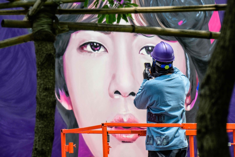 An artist refers to their phone for reference during the spray painting of a mural of K-pop megastars BTS in Seoul on June 12, 2023. (Photo by Anthony Wallace / AFP)