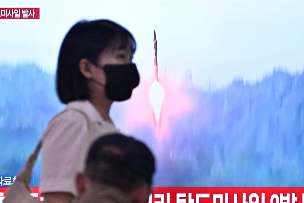 A woman walks past a television showing a news broadcast with file footage of a North Korean missile test, at a railway station in Seoul on June 15, 2023. (Photo by Anthony WALLACE / AFP)