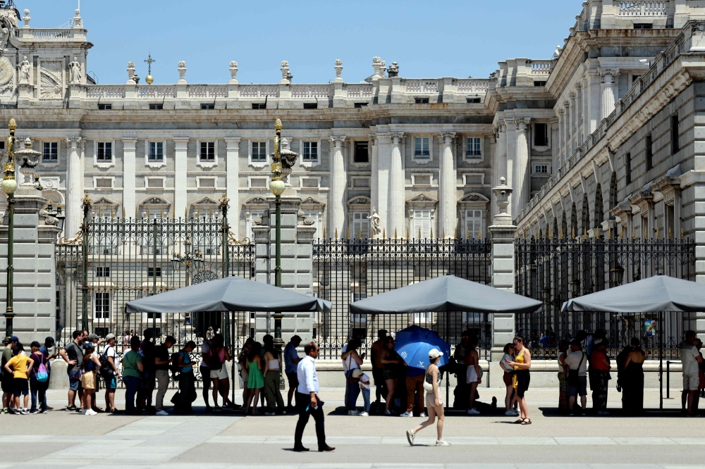 Tourists protect themselves of the sun while they visit the Royal Palace in Madrid city centre under very high temperatures, on June 26, 2023 as Spain is facing its first heatwave of the summer, with temperatures expected to exceed 44 degrees locally in the south of the country. (Photo by Thomas Coex / AFP)