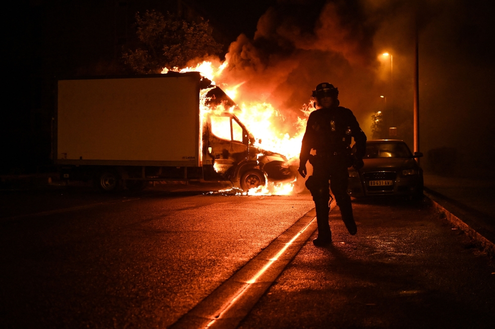 A French anti-riot police officer walk past a burning truck in Nantes, western France on early July 1, 2023. Photo by Sebastien SALOM-GOMIS / AFP
