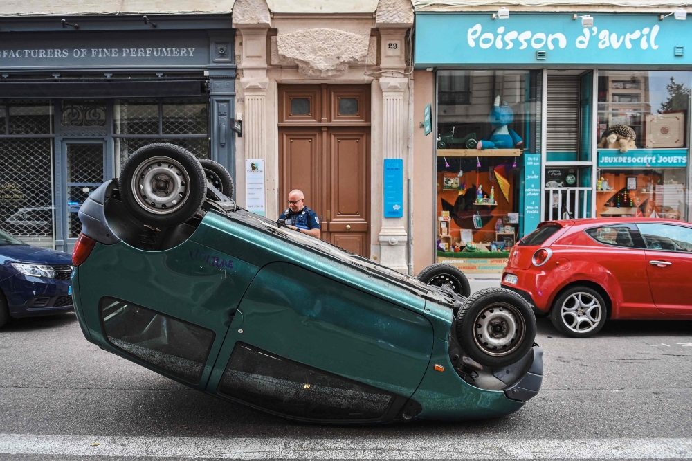 A police officer stands by a car which is upside down on a street following a fourth consecutive night of rioting in France sparked by the death of teenage driver Nahel by a police bullet, in Lyon, south-eastern France on July 1, 2023. Photo by OLIVIER CHASSIGNOLE / AFP)
