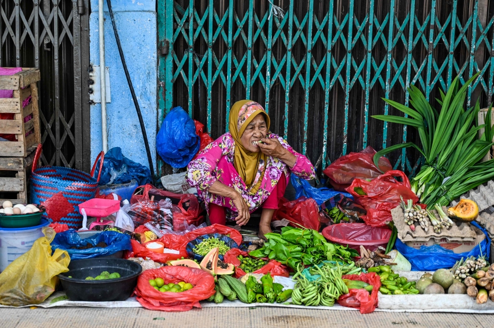 A woman eats a snack while waiting for costumers at a market in Banda Aceh on July 3, 2023. (Photo by CHAIDEER MAHYUDDIN / AFP)
