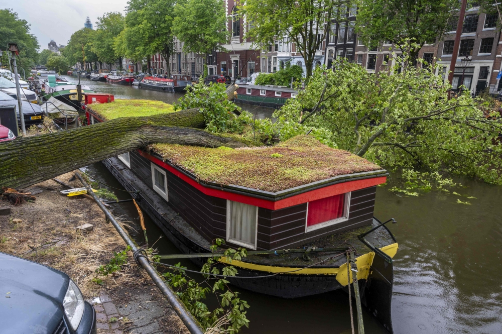 A storm damaged tree lies on a canal boat on the Keizersgracht in the centre of Amsterdam on July 5, 2023, after winds of ' Storm Poly' struck north Holland where a 'code red' was issued as an extreme weather warning. (Photo by Evert Elzinga / ANP / AFP)