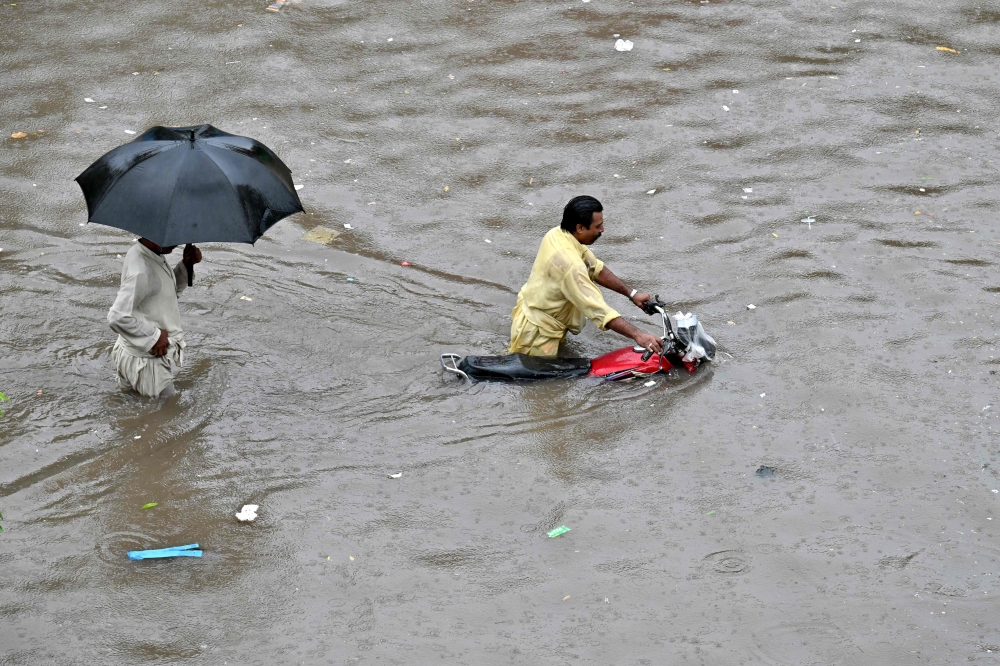 A motorcyclist pushes his bike through a flooded street after heavy rainfall in Lahore on July 5, 2023. (Photo by Arif Ali / AFP)