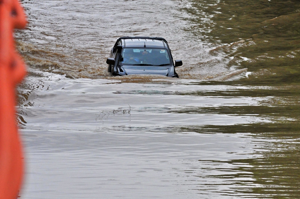 A commuter drives his car through a flooded road after heavy monsoon rains in Gurgaon on July 9, 2023. (Photo by Vinay Gupta / AFP)