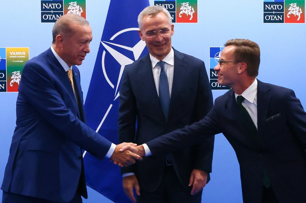 Turkish President Tayyip Erdogan (left) and Swedish Prime Minister Ulf Kristersson shake hands in front of NATO Secretary-General Jens Stoltenberg prior to their meeting, on the eve of a NATO summit, in Vilnius on July 10, 2023. (Photo by YVES HERMAN / POOL / AFP)