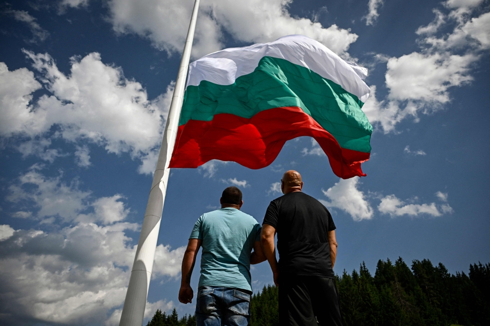 People watch the rising of a large Bulgarian flag during preparations ahead of the inauguration of an 111 m / 364 ft flagpole at Rozhen meadows near the city of Smolyan, some 80km south of Plovdiv, on July 13, 2023. (Photo by Nikolay Doychinov / AFP)