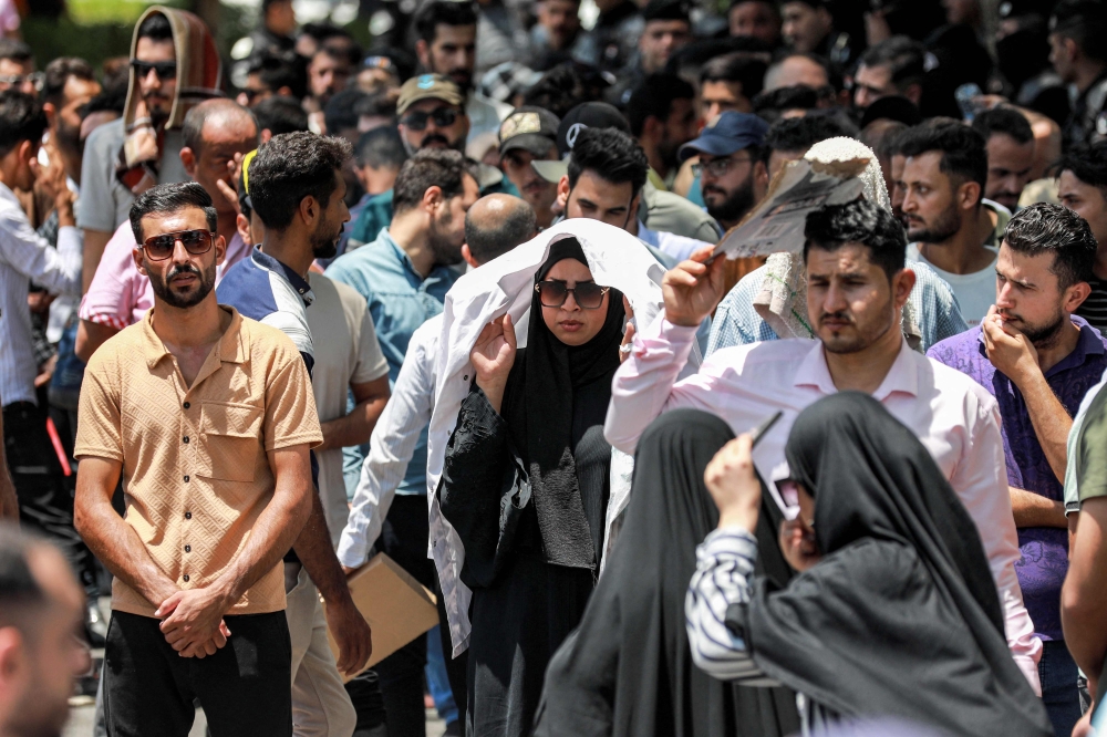 Protesters shade themselves as they march at a demonstration against water scarcity and power outages in Baghdad on July 18, 2023 during a heat wave. (Photo by Murtaja LATEEF / AFP)
