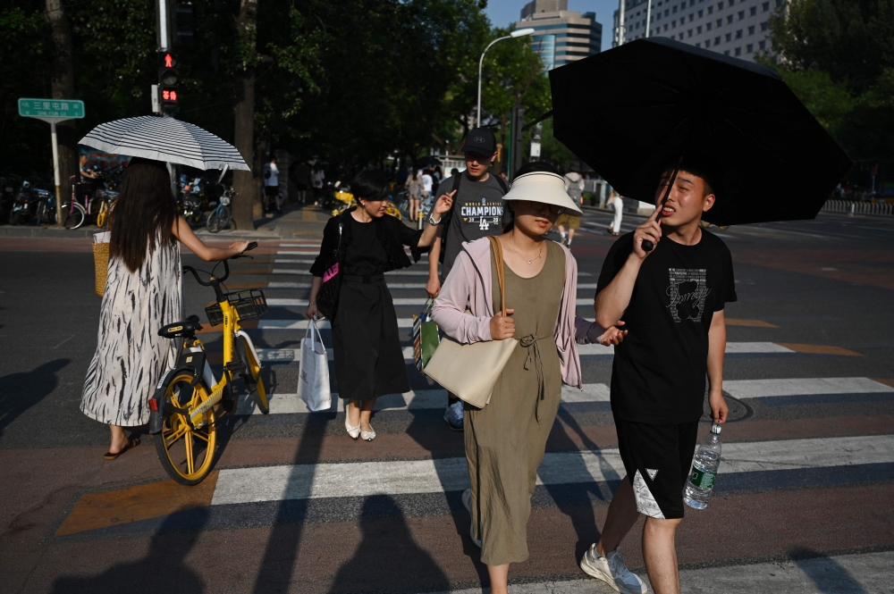 People shelter under umbrellas during heatwave conditions in Beijing on July 19, 2023. (Photo by Greg Baker / AFP)