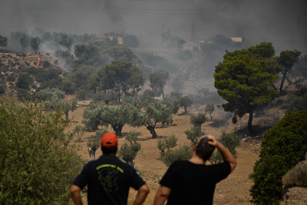 A firefighter (L) and a local resident react as they look at a wildfire in a forest near Nea Peramos, west of Athens on July 19, 2023. (Photo by Louisa Gouliamaki / AFP)