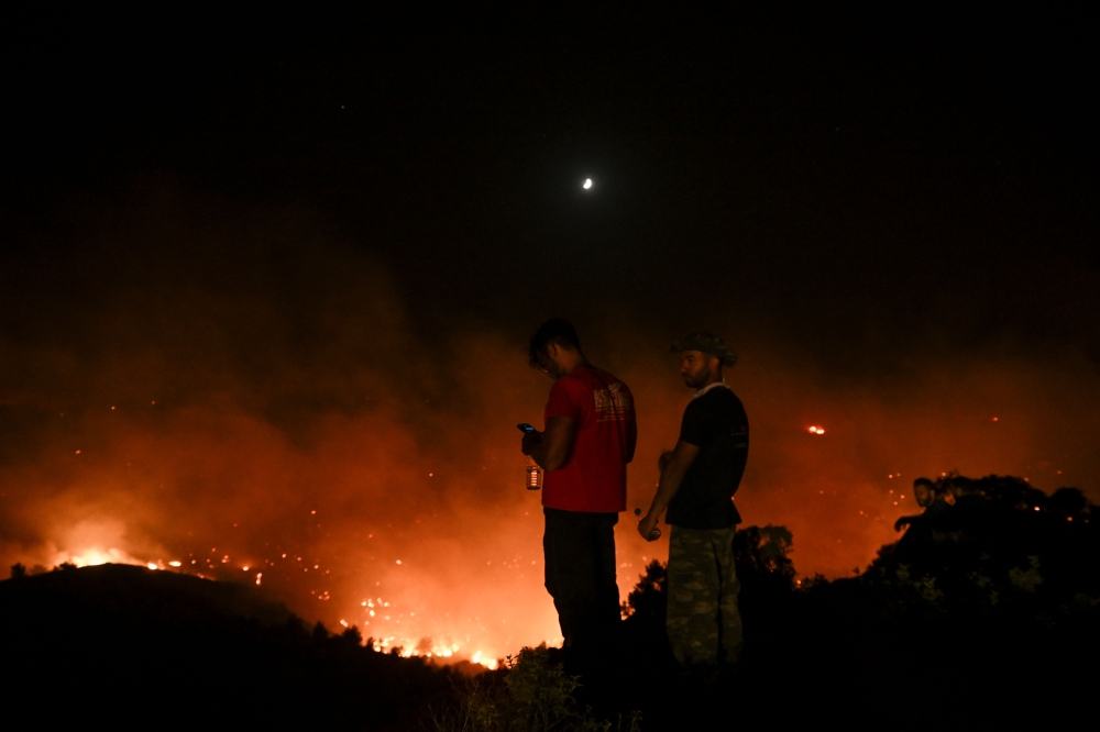 People watch the fires near the village of Malona in the Greek island of Rhodes on July 23, 2023. (Photo by Spyros Bakalis / AFP)