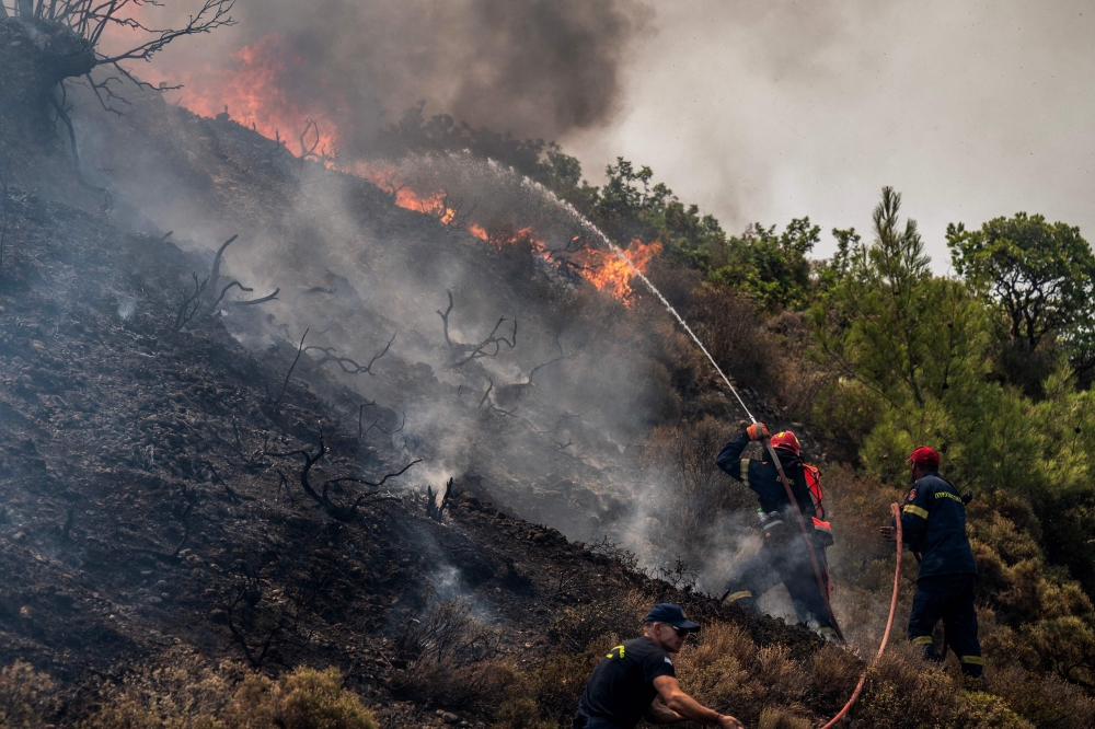 Firefighters use a hose as they take part in an operation against a fire near Vati, on the Greek Aegean island of Rhodes on July 26, 2023. Photo by Angelos Tzortzinis / AFP