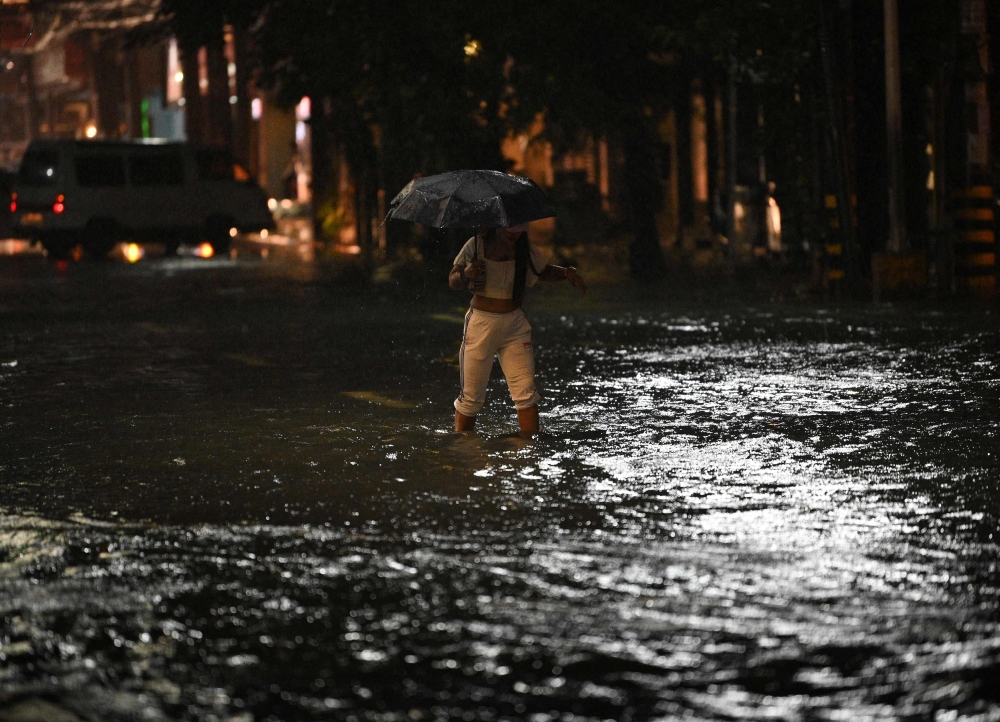 This photo taken July 29, 2023 shows a pedestrian wading a flooded street of Manila as Tropical Storm Khanun intensifies the southwest monsoon rain. (Photo by Ted Aljibe / AFP)