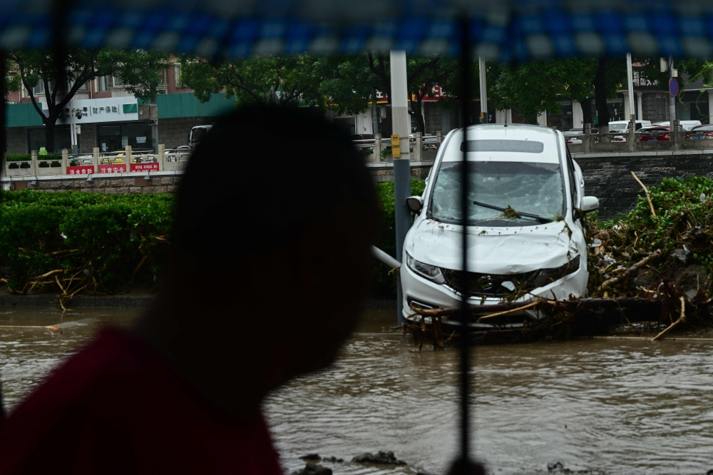 A man walks past a damaged car after heavy rains in Mentougou district in Beijing on August 1, 2023. Photo by Pedro PARDO / AFP