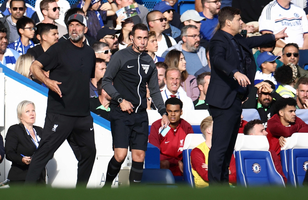 Fourth Official David Coote (C) stands betweeen Liverpool's German manager Jurgen Klopp (L) and Chelsea's Argentinian head coach Mauricio Pochettino during the English Premier League football match between Chelsea and Liverpool at Stamford Bridge in London on August 13, 2023. (Photo by HENRY NICHOLLS / AFP)
