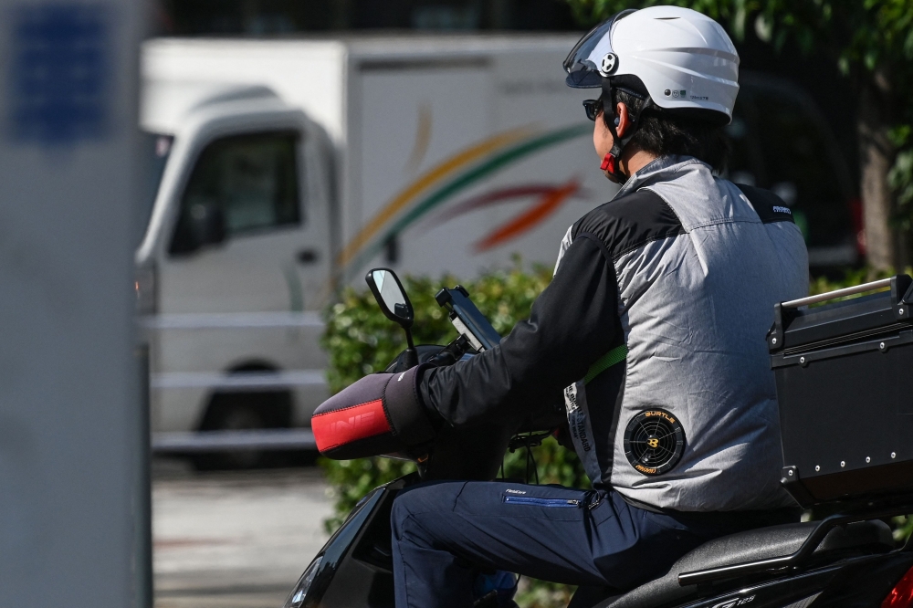This photo taken on August 4, 2023 shows a man wearing a jacket with battery-powered built-in fans to keep cool in the heat as he sits on his motor scooter along a street in Tokyo. (Photo by Richard A. Brooks / AFP) 