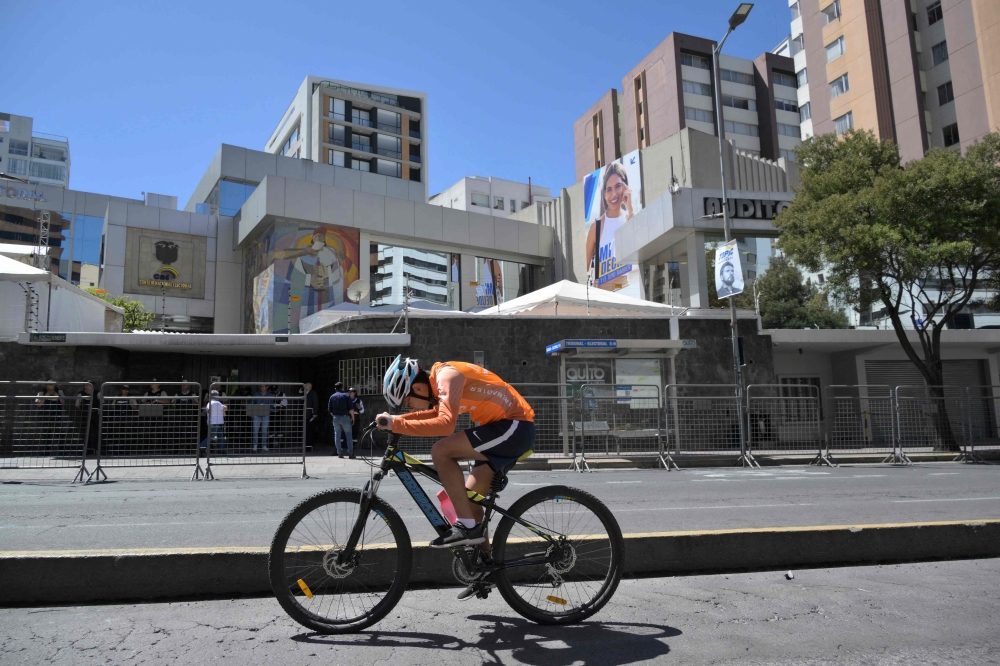 A man rides a bicycle outside the National Electoral Council in Quito, on August 18, 2023. Amid the commotion over the shooting death of a candidate and violence linked to drug trafficking, Ecuador will vote this Sunday in early elections to elect a new president and put an end to an institutional crisis. (Photo by Rodrigo BUENDIA / AFP)
