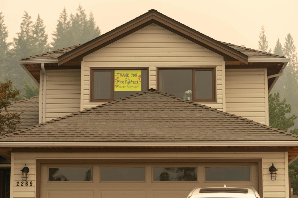 A “thank you all firefighters” sign is put in the front window of a house near Shannon Lake as the nearby McDougall Creek wildfires continue in West Kelowna, British Columbia on August 19, 2023. (Photo by Paige Taylor White / AFP)