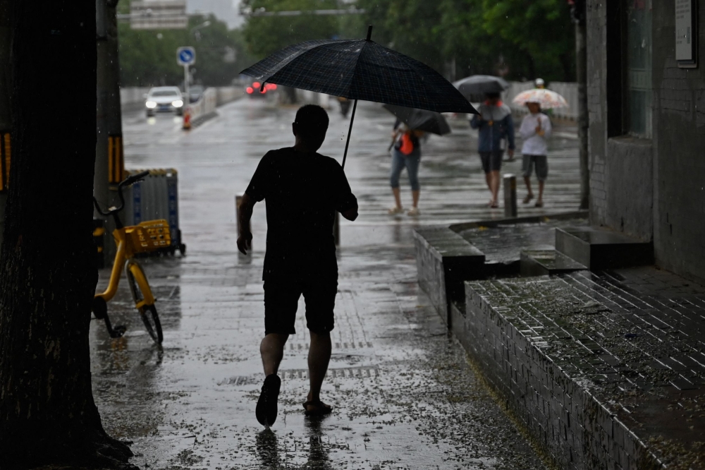 A man shelters from the rain with an umbrella in Beijing on July 30, 2023. (Photo by Pedro Pardo / AFP)

