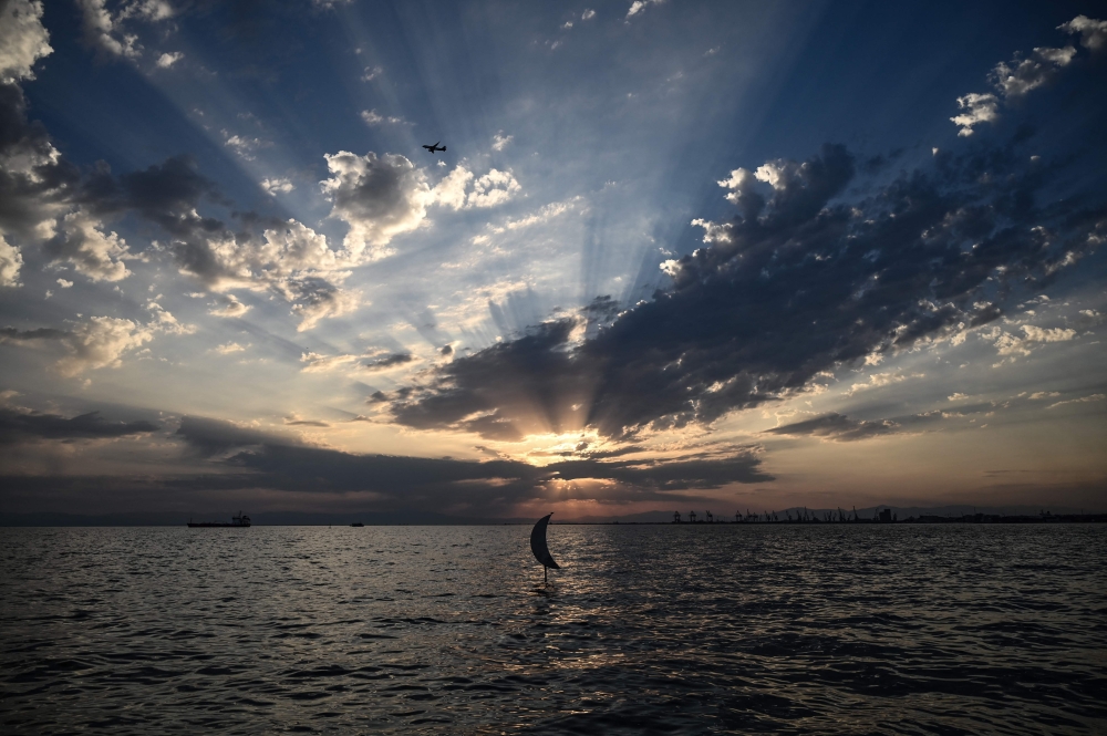 A sculpture of a moon crescent, created by the artist Pavlos Vasileiadis, is displayed at sunset along the waterfront of Thessaloniki on August 20, 2023. Photo by Sakis MITROLIDIS / AFP