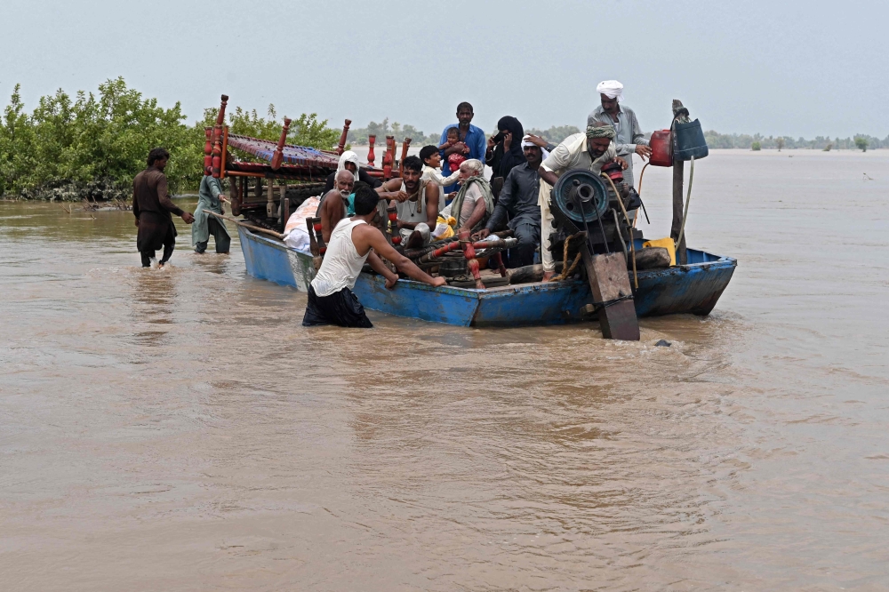 People with their belongings wade through the flood affected area of Chanda Singh Wala village in Kasur district on August 22, 2023. (Photo by Arif ALI / AFP)