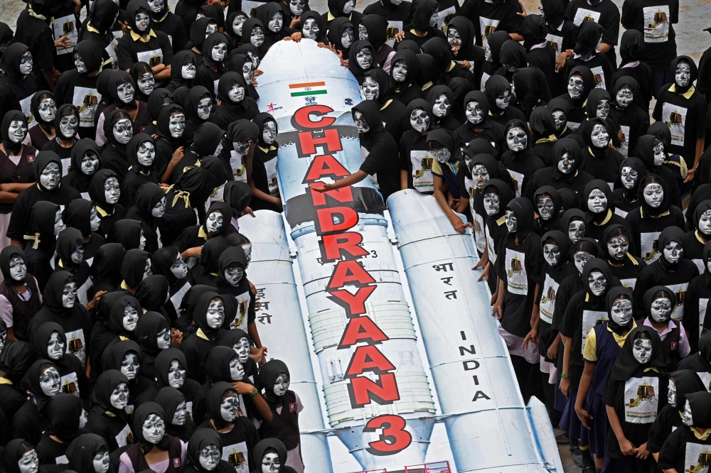 Students with painted faces surround a replica of the Chandrayaan-3 spacecraft in Chennai on August 22, 2023. (Photo by R.Satish Babu / AFP)