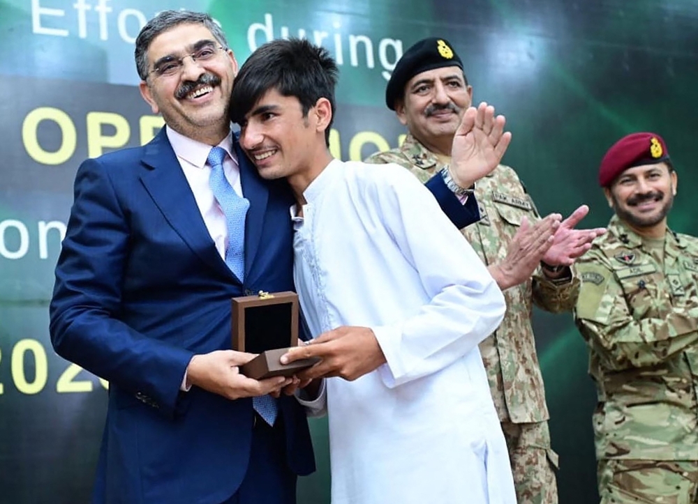 This handout photo taken and released by Pakistan's Press Information Department on August 24, 2023, shows Pakistani caretaker Prime Minister Anwaar-ul-Haq Kakar (left) greets a survivor of the cable car accident during a ceremony in honor of rescuers efforts in cable car accident at the Prime Minister office in Islamabad. (Photo by Pakistan PRESS INFORMATION DEPARTMENT / AFP)