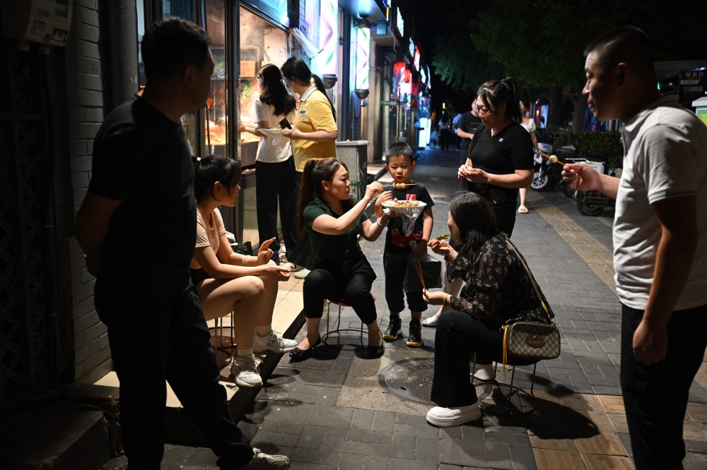 A family eats snacks outside a restaurant in Beijing on August 26, 2023. (Photo by GREG BAKER / AFP)
