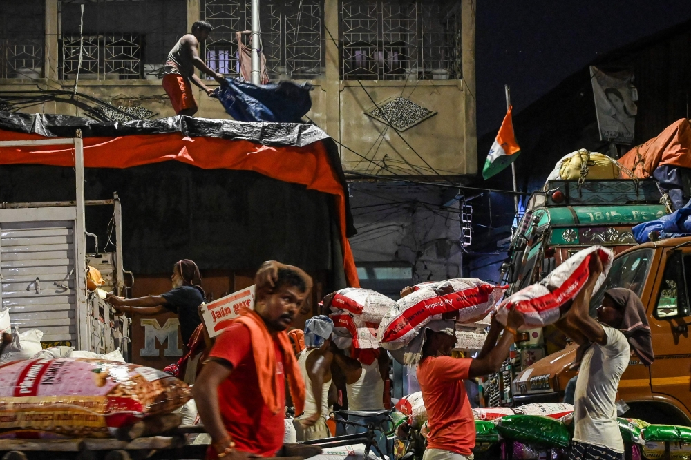 Workers load a truck with sacks of grains and other items to be sent to retail outlets across the city, at a wholesale market in Kolkata on August 31, 2023. Photo by DIBYANGSHU SARKAR / AFP