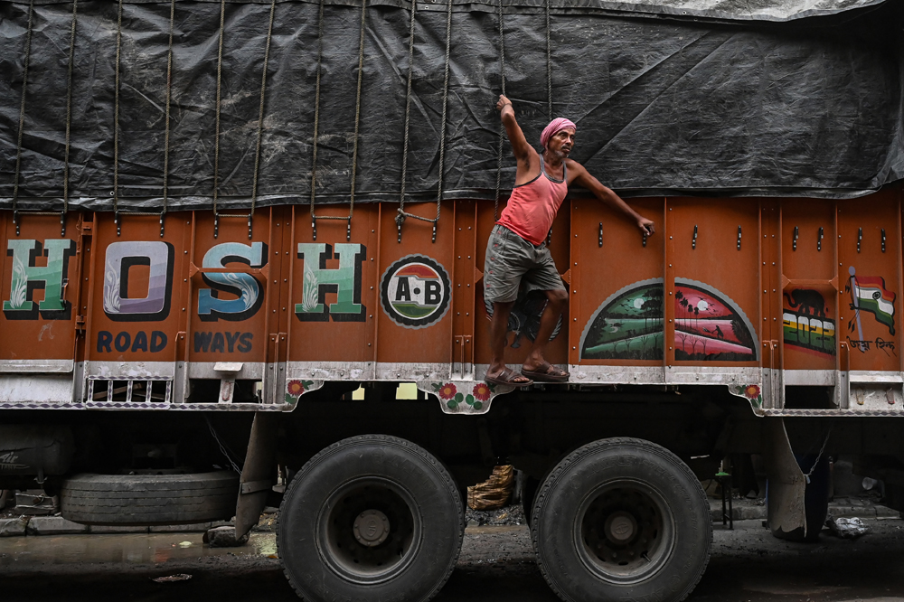 A worker ties rope around a loaded truck transporting food grains and other products to retail outlets across the city, at a wholesale market in Kolkata on August 31, 2023. Photo by DIBYANGSHU SARKAR / AFP