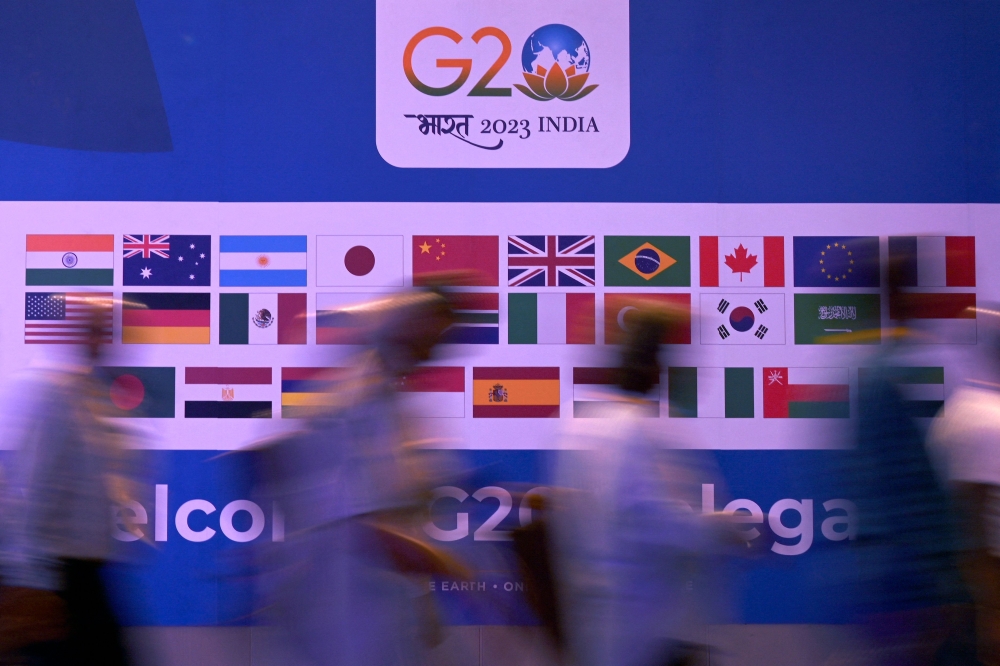 People walk past a banner with flags of countries participating in G20 summit at the International Media Center (IMC) at G20 venue on the eve of the two-day G20 summit in New Delhi on September 8, 2023. (Photo by Tauseef Mustafa / AFP)